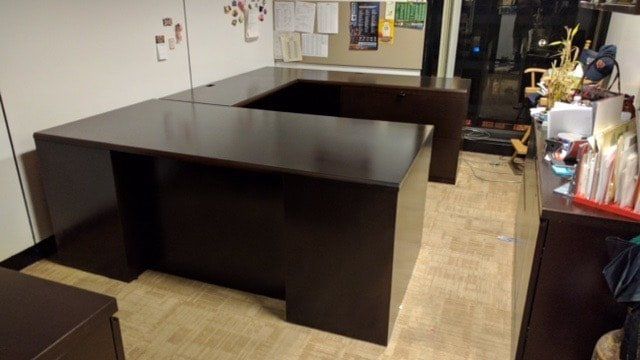 A dark wooden desk in a room with a bulletin board behind it