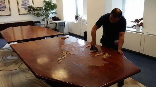 A man is cleaning a wooden table in a room