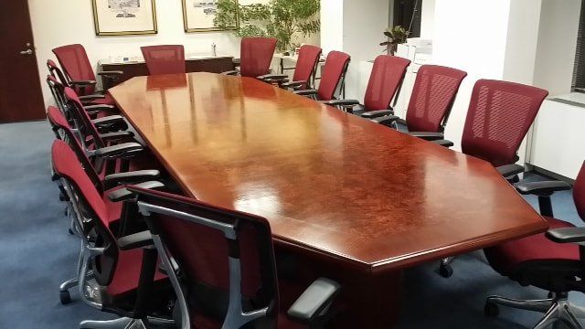 A conference room with a long table and red chairs