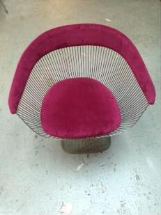 A wire chair with a pink cushion is sitting on a concrete floor.
