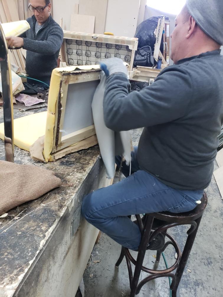 A man is sitting on a stool working on a chair
