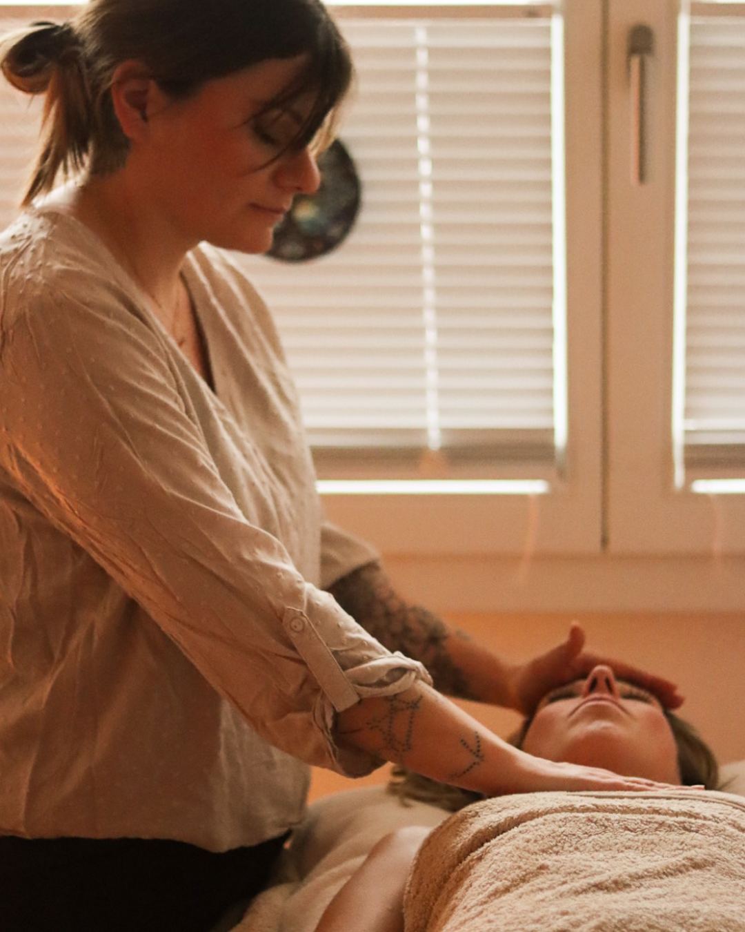 Une femme prodigue des soins énergétiques à une autre femme allongée sur une table. Ses mains sont posées sur son front et sa poitrine.