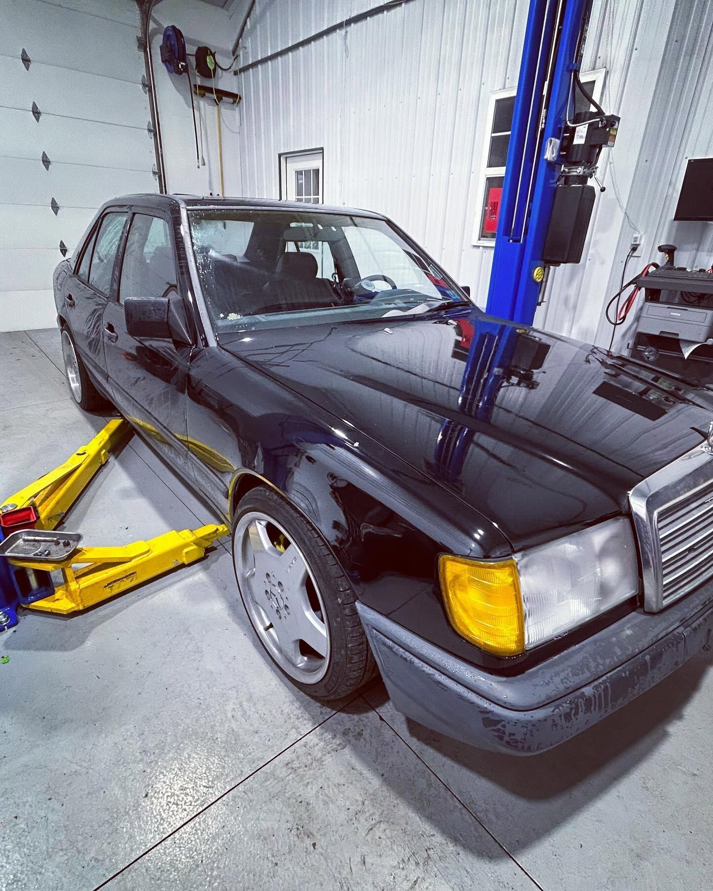Black sedan on a lift in an auto repair shop, with a yellow floor jack nearby. | Pommerer's Automotive