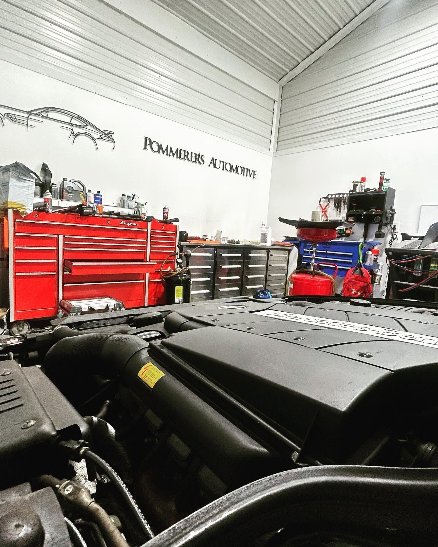Auto repair workshop with red tool cabinets and machinery under a white metal ceiling. | Pommerer's Automotive