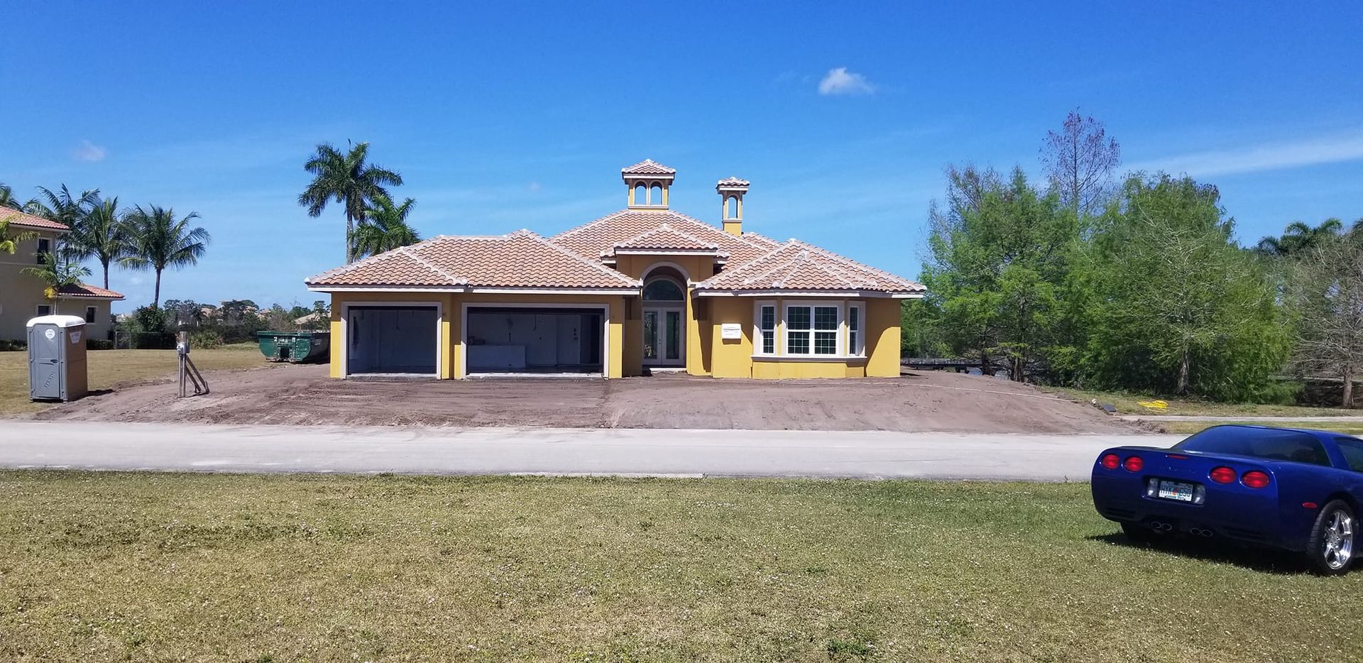 A blue car is parked in front of a yellow house