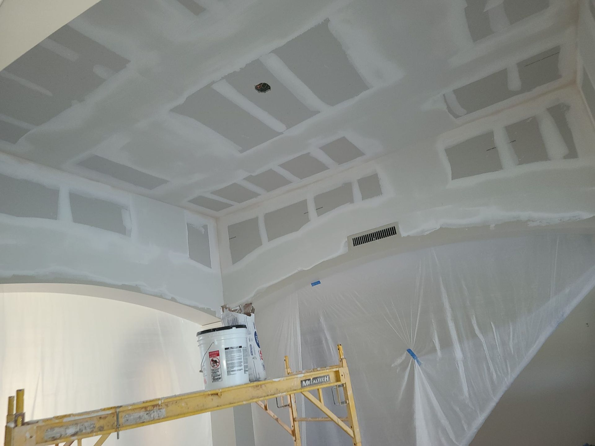 A man is painting the ceiling of a room with a ladder.