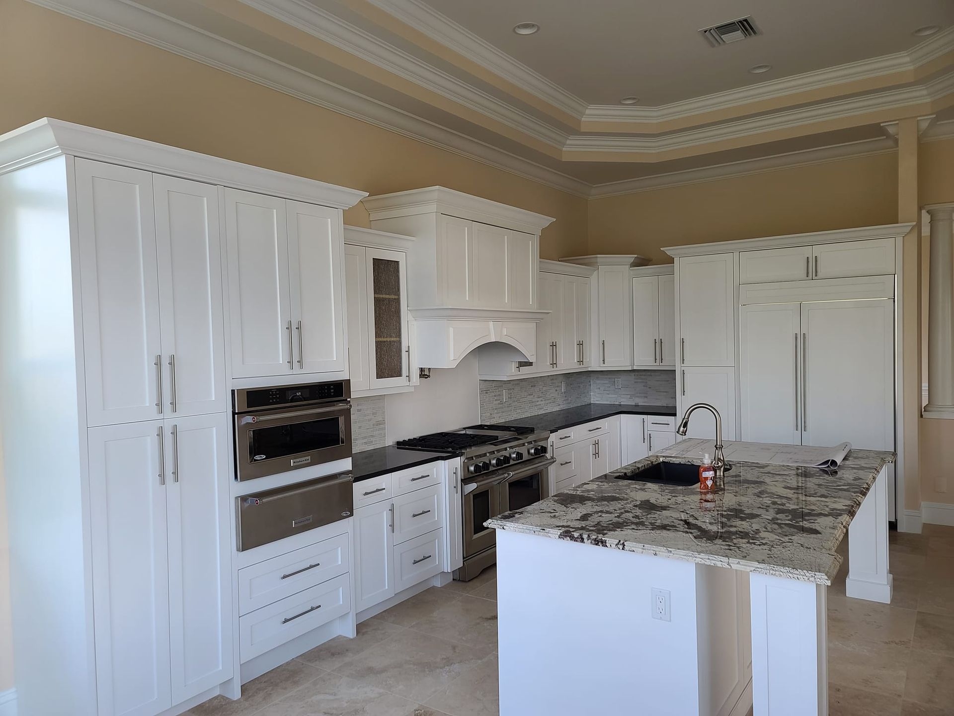 A kitchen with white cabinets , granite counter tops , stainless steel appliances and a large island.
