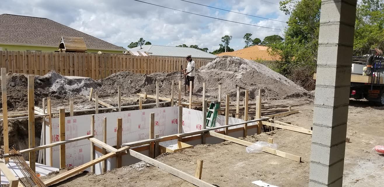 A man is standing in the dirt in front of a house under construction.
