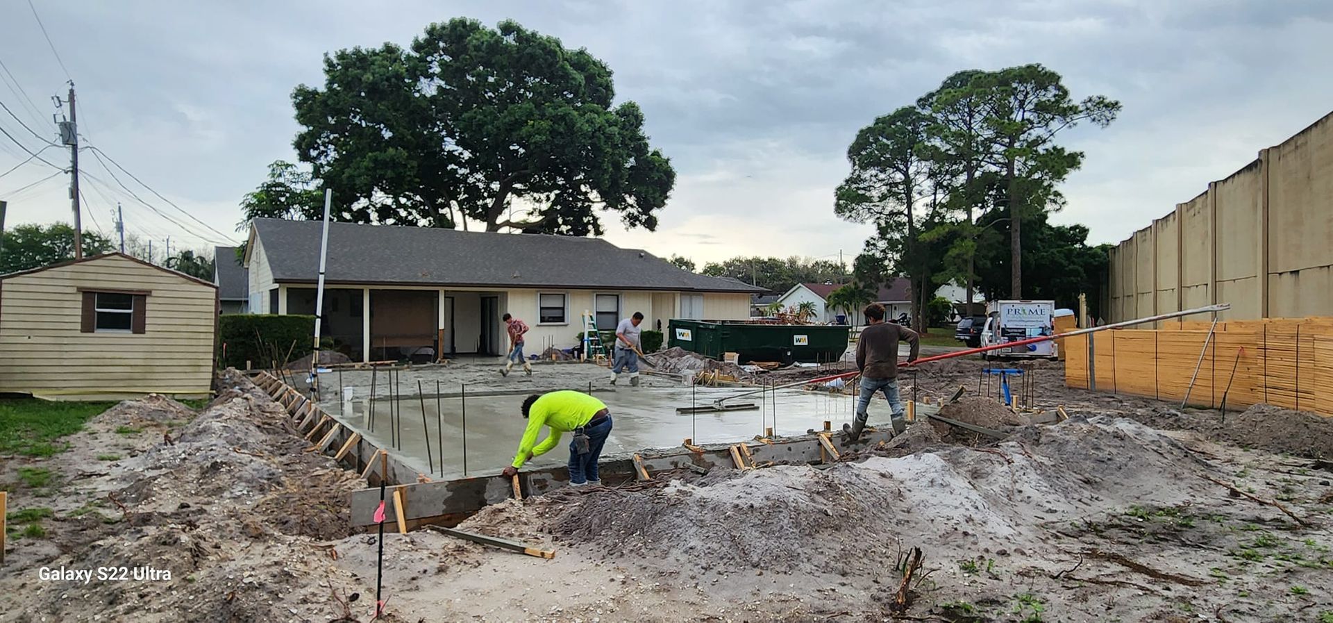 A group of construction workers are working in a muddy area in front of a house.