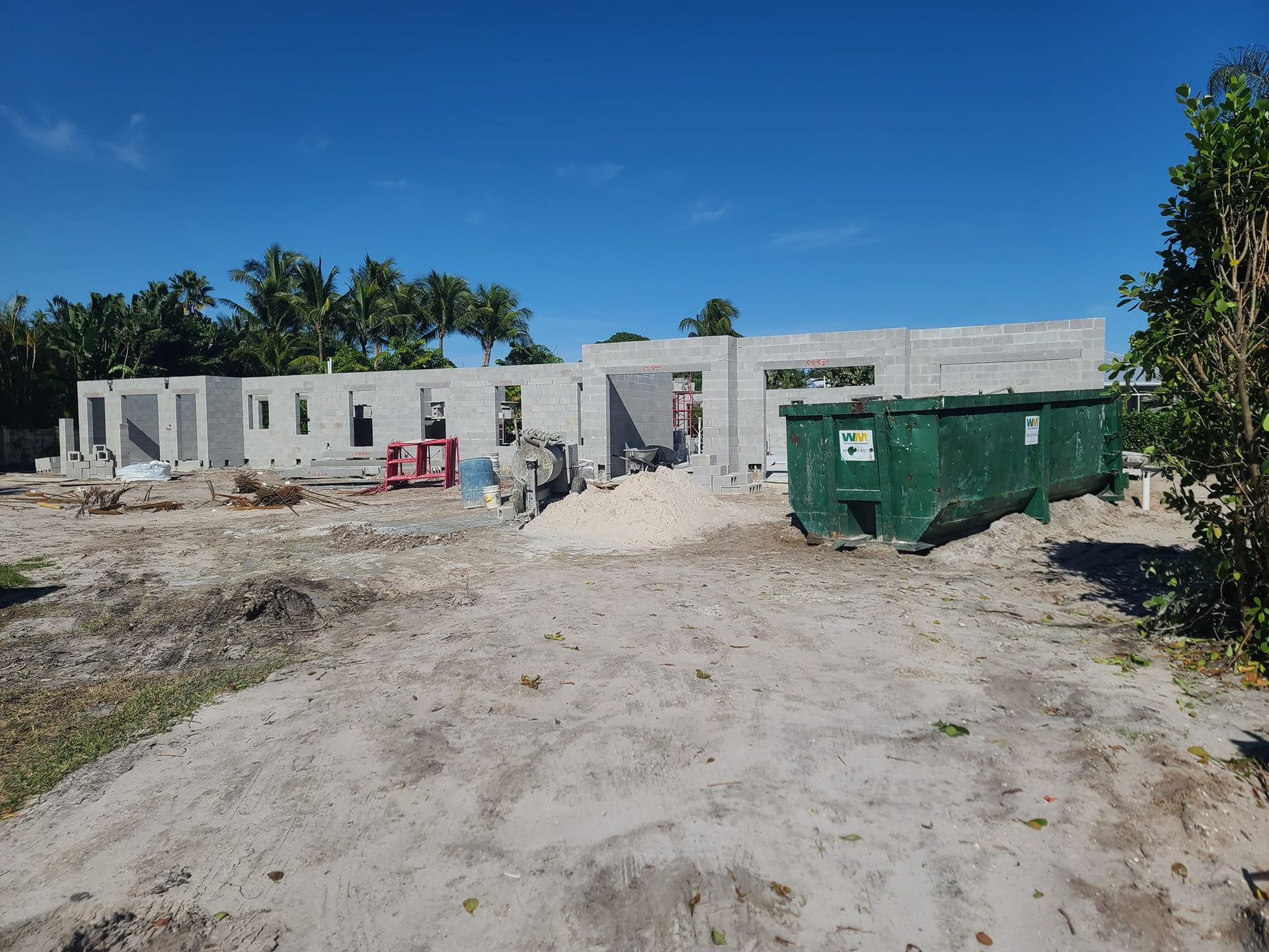 A large green dumpster sits in front of a building under construction