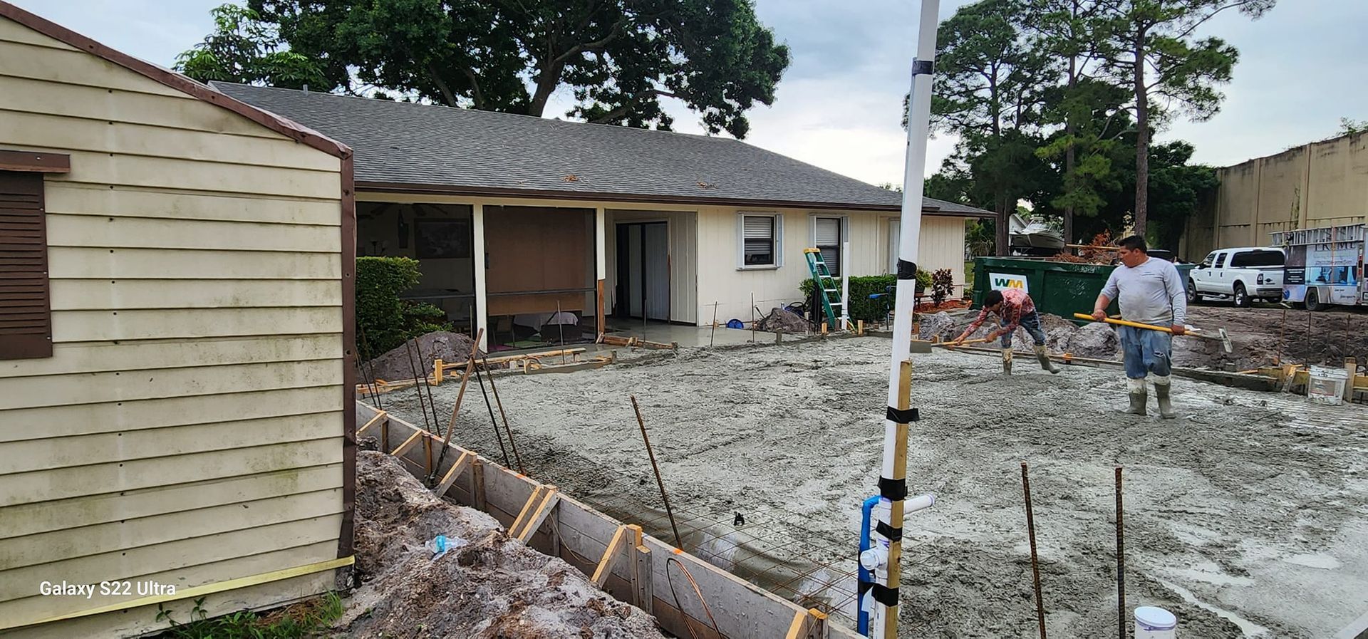 A group of people are working on a concrete driveway in front of a house.