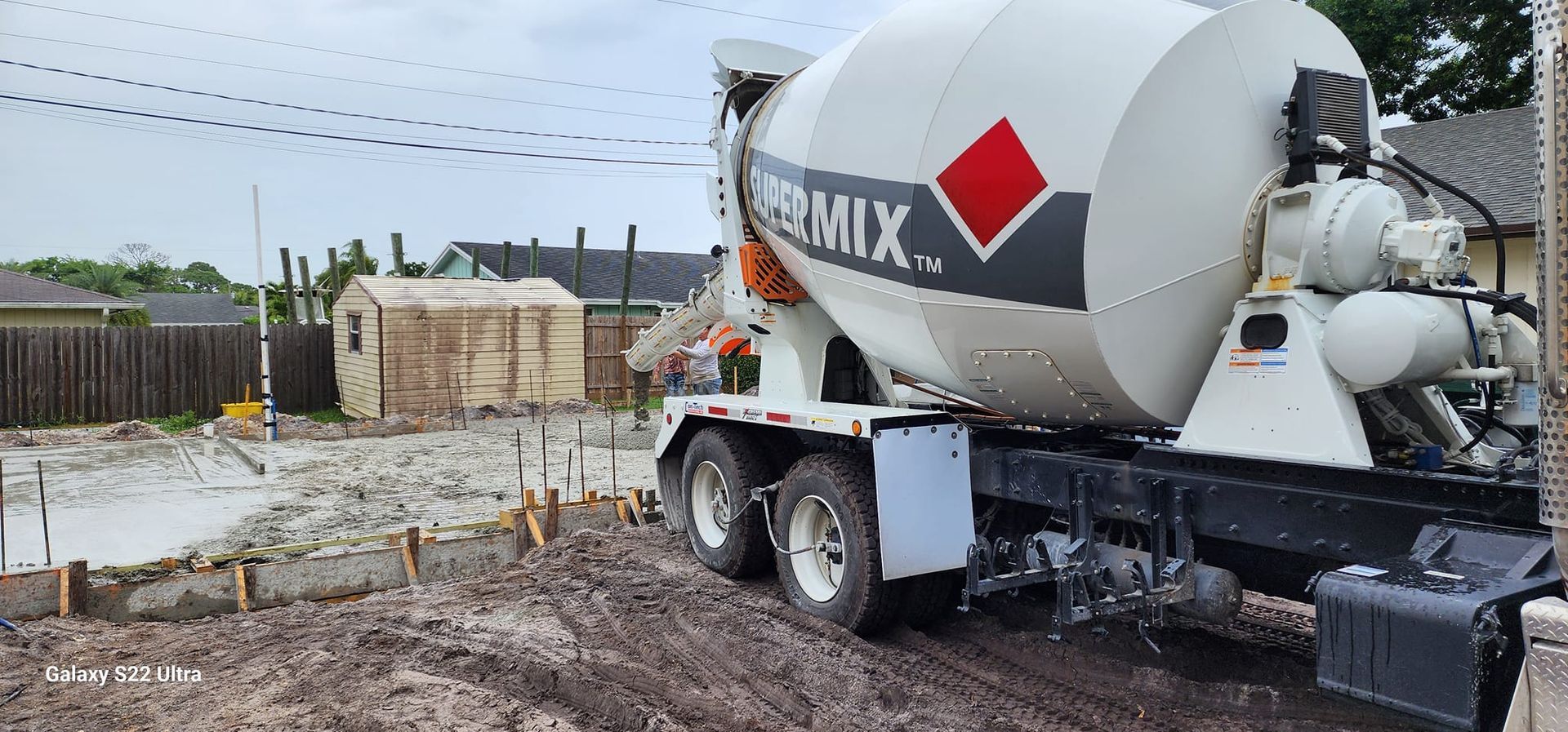 A concrete mixer truck is driving down a dirt road.