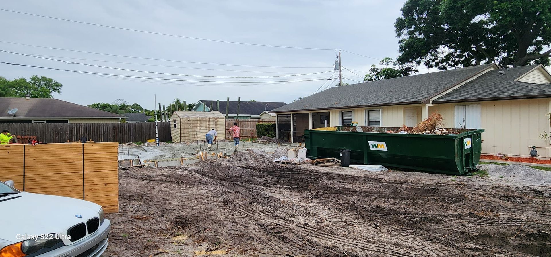 A dumpster is sitting in the dirt in front of a house under construction.