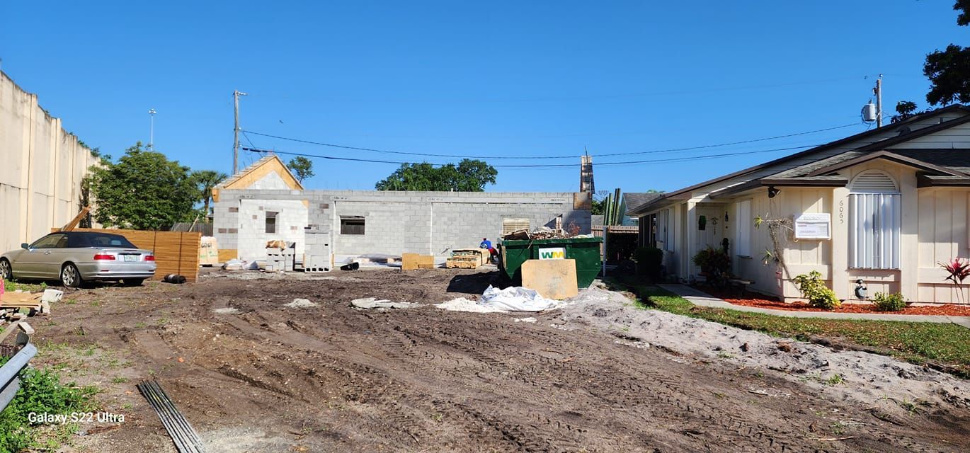 A car is parked in the dirt in front of a house.