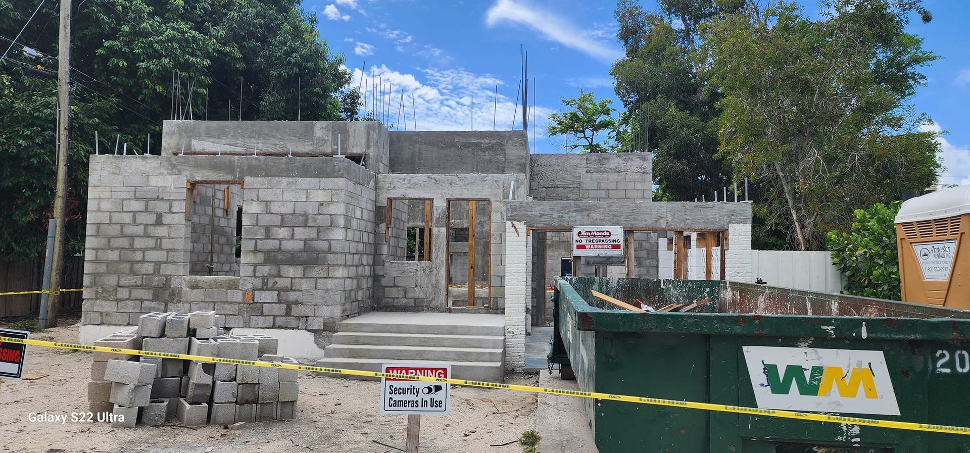 A house is being built with a green dumpster in front of it.
