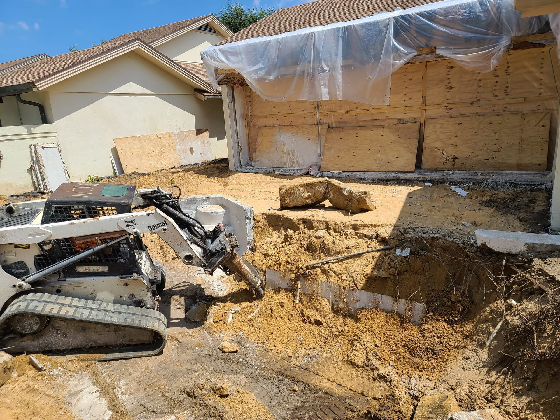 A bulldozer is digging a hole in the dirt in front of a house.