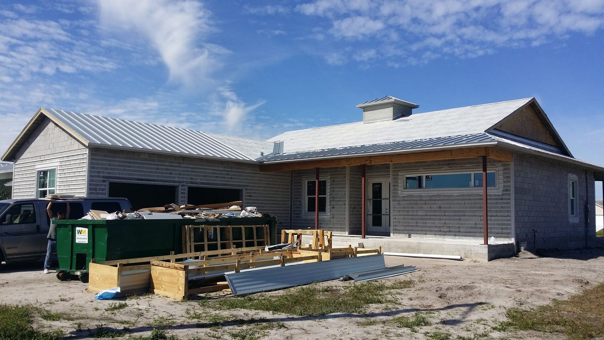 A house under construction with a green dumpster in front of it.