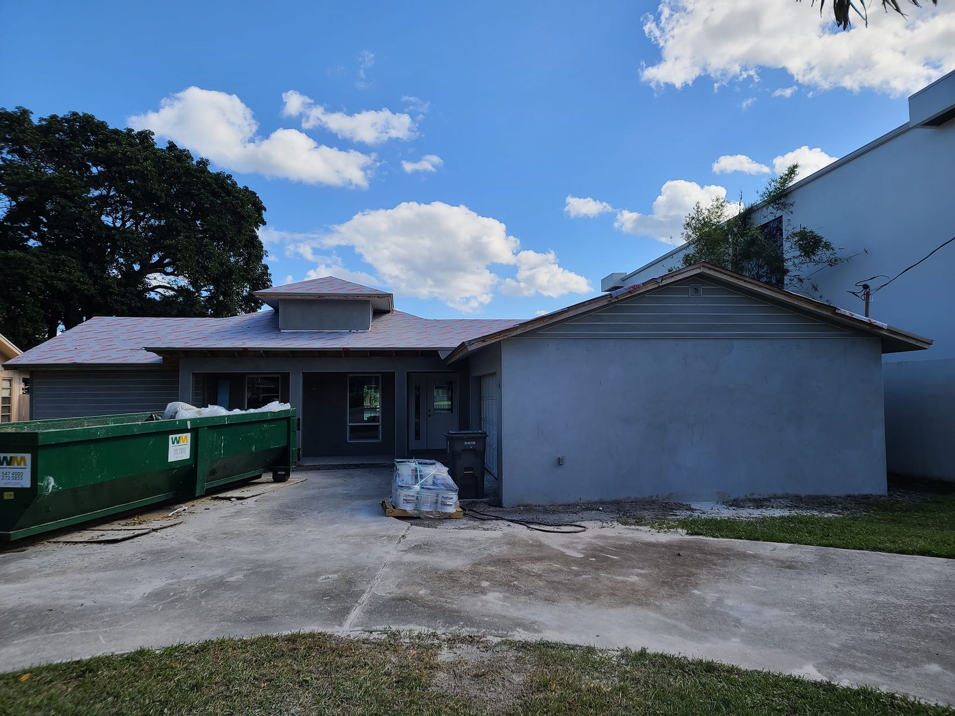 A house under construction with a green dumpster in front of it.
