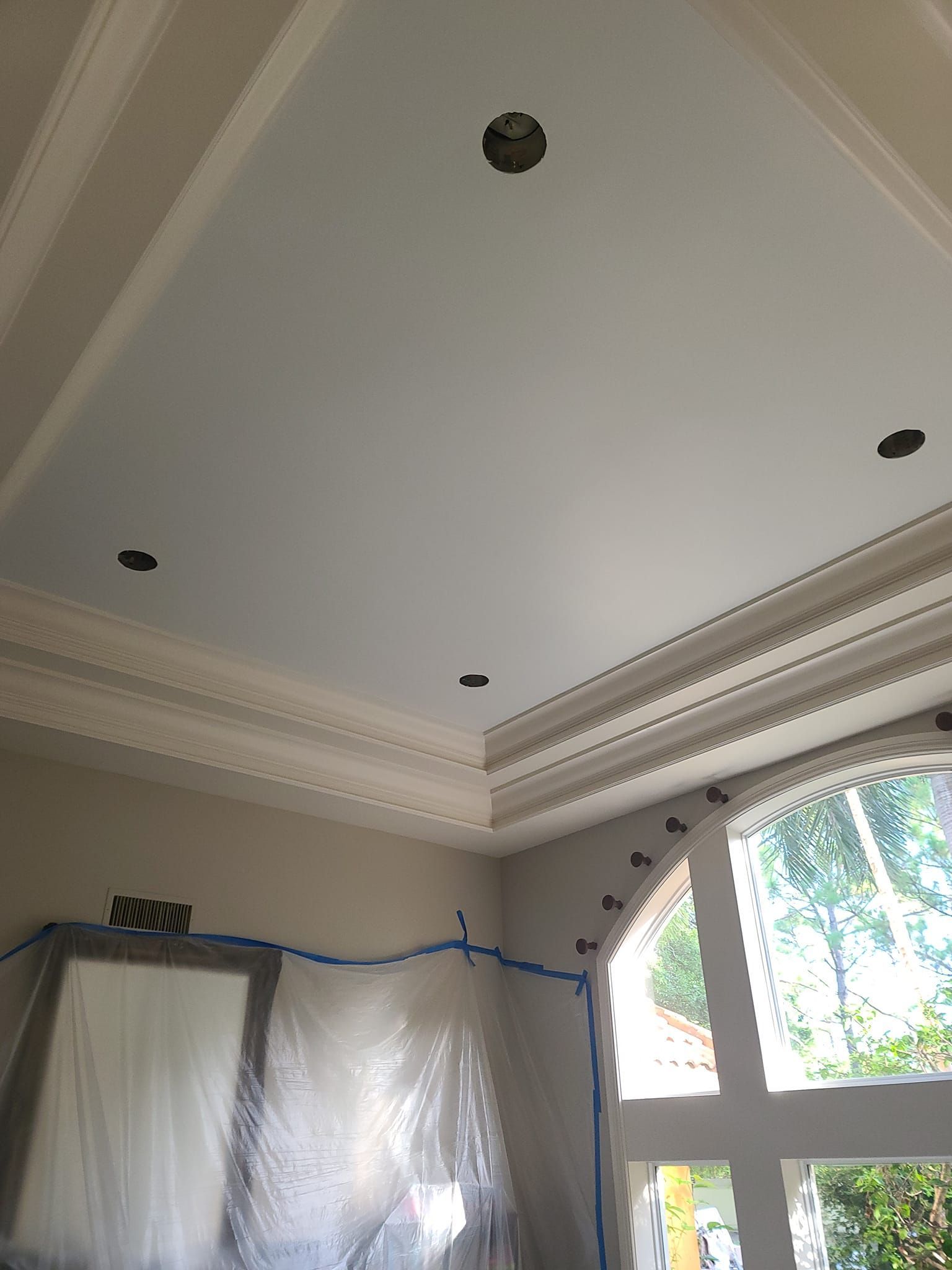 A room with a ceiling that is being painted and a window.