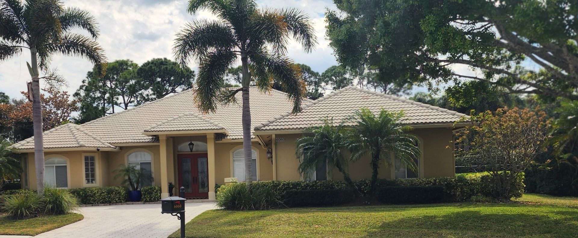A light yellow house with a tile roof, palm trees, and green lawn.