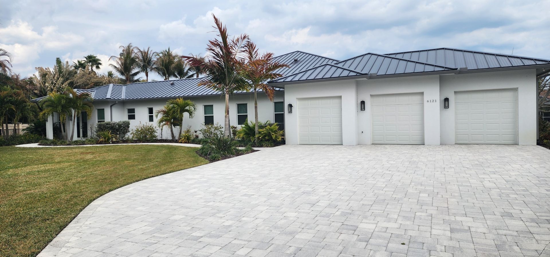 White house with grey roof and three-car garage, with a stone driveway and a green lawn.