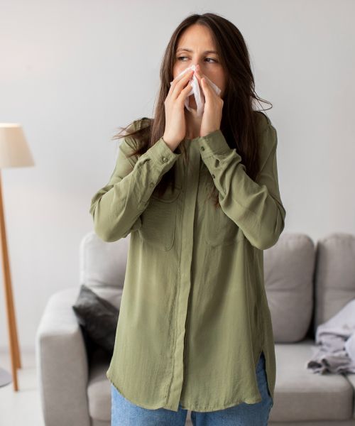 A woman in a green shirt is blowing her nose in a living room.