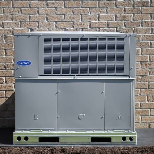 A carrier air conditioner is sitting in front of a brick wall