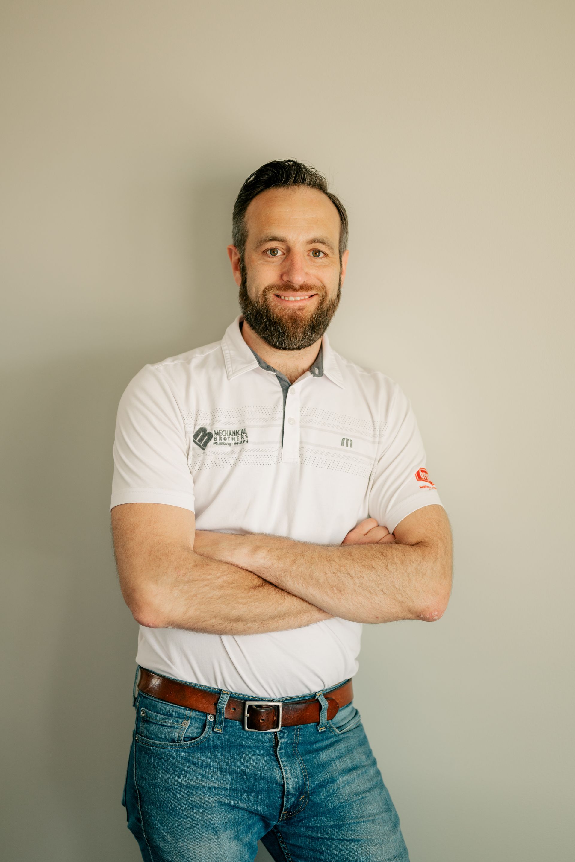 A man with a beard is standing with his arms crossed in front of a wall.