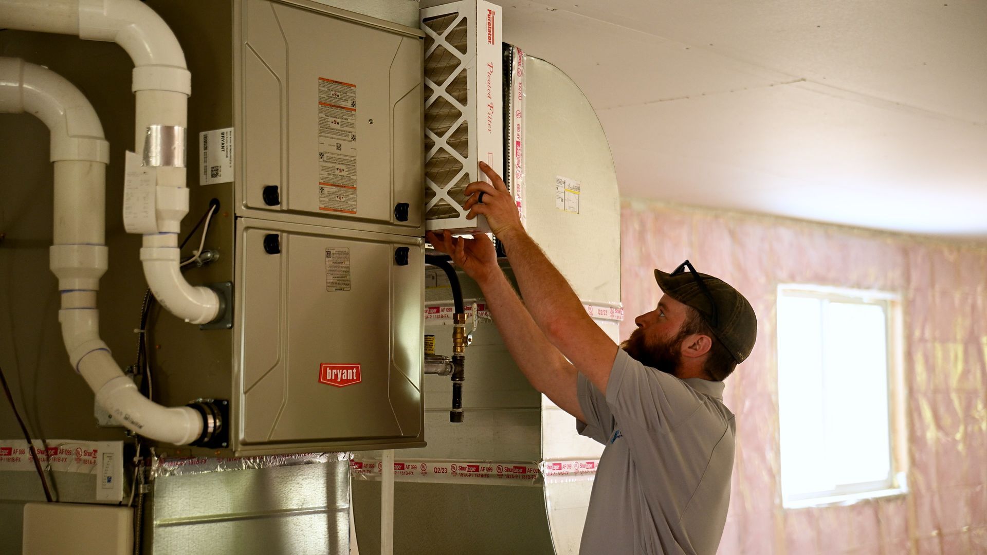 A man is working on an air conditioner in a basement.