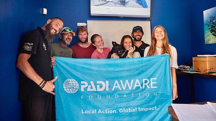 Group of people holding a blue PADI AWARE Foundation banner inside a room with blue walls.