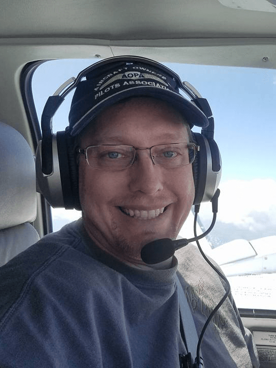 Man in airplane cockpit wearing headset, smiling.