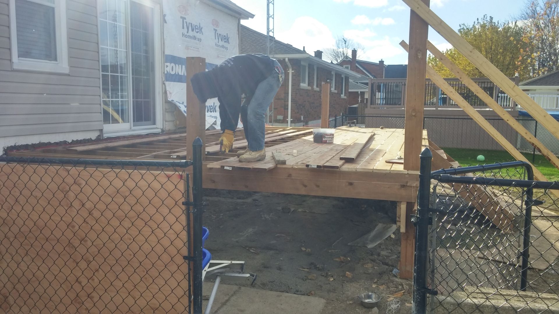 A man is working on a wooden deck in front of a house.