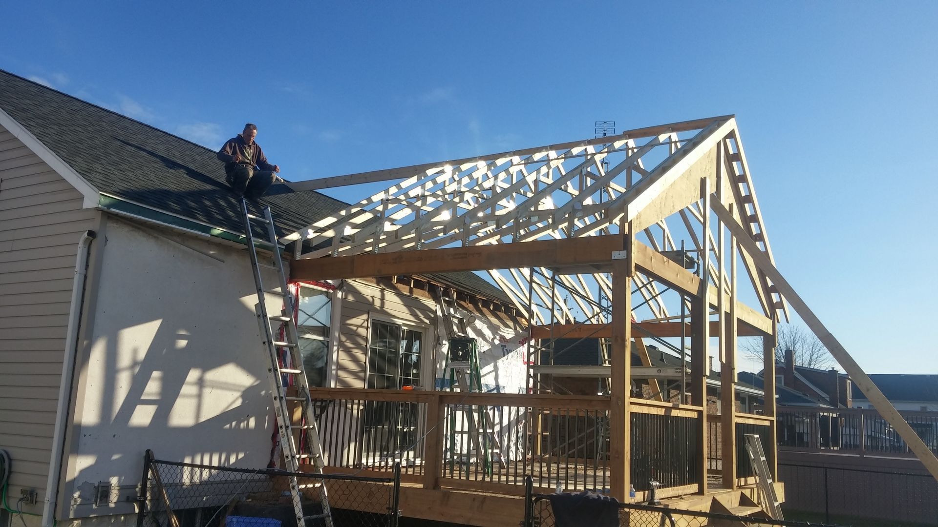 A man on a ladder is working on the roof of a house under construction.