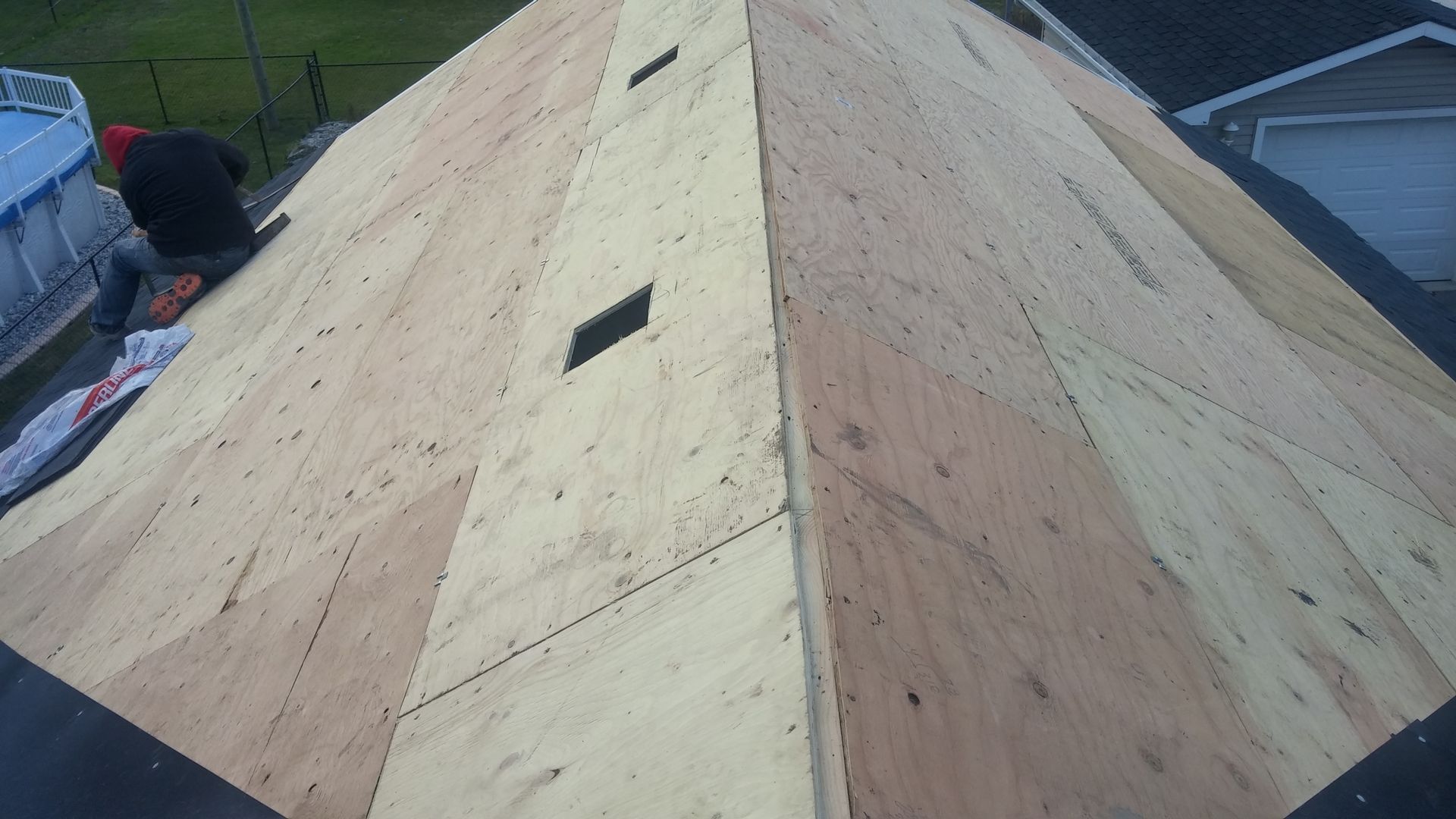 A man is working on a roof that is covered in plywood.