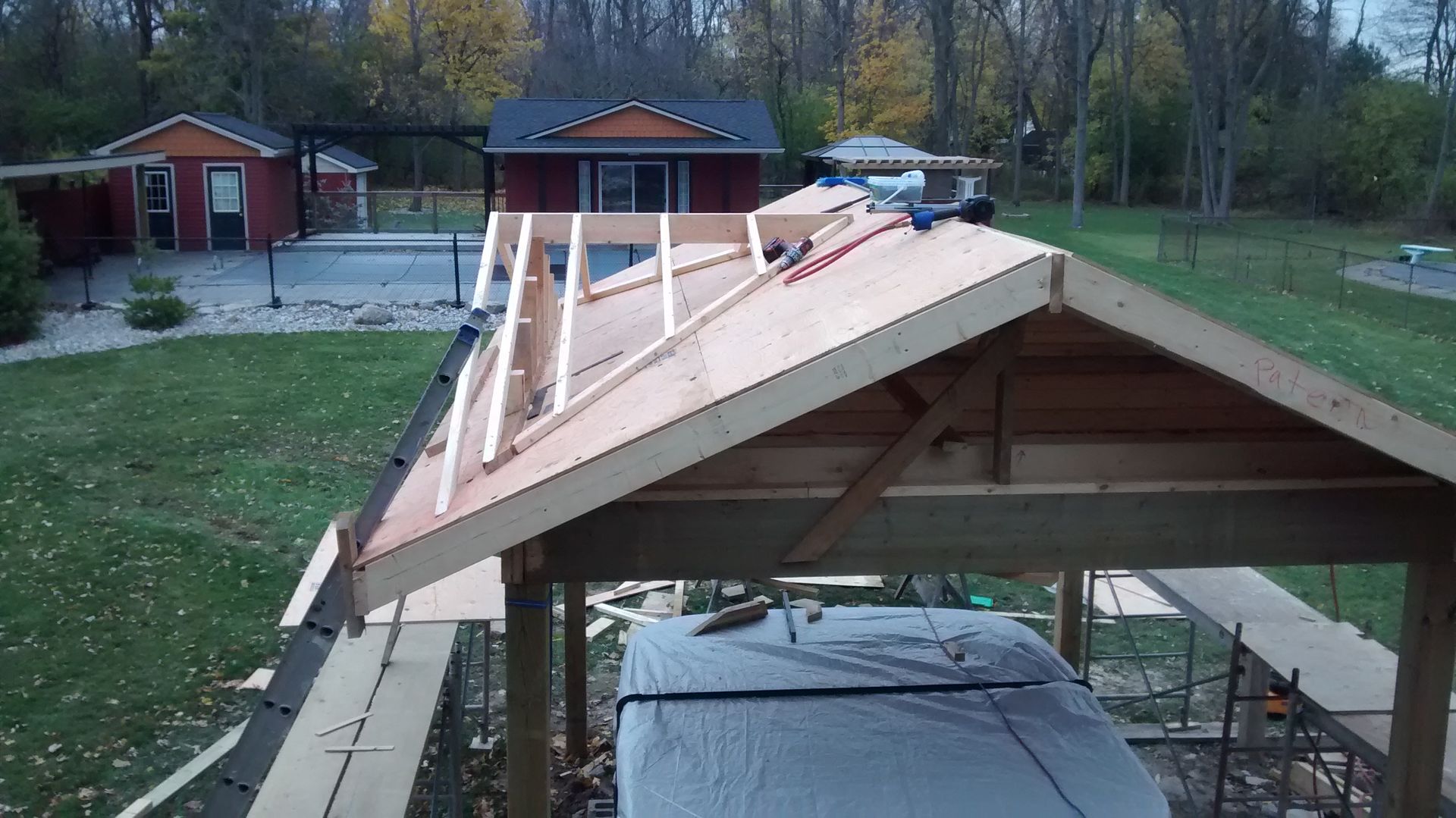 A roof is being built in a backyard with a house in the background