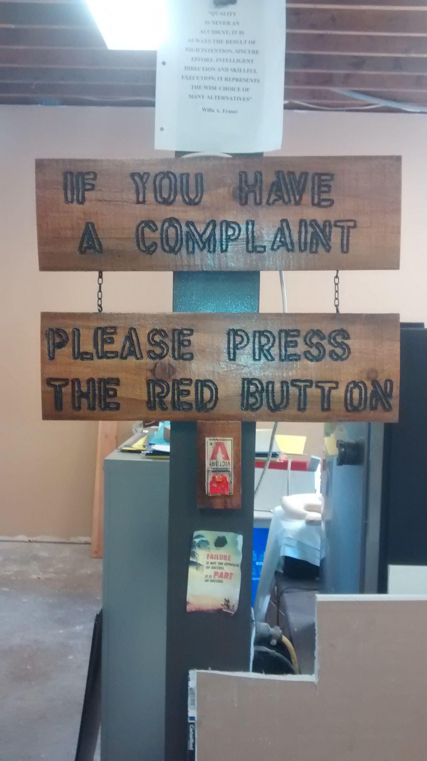 A wooden sign that says if you have a complaint please press the red button.