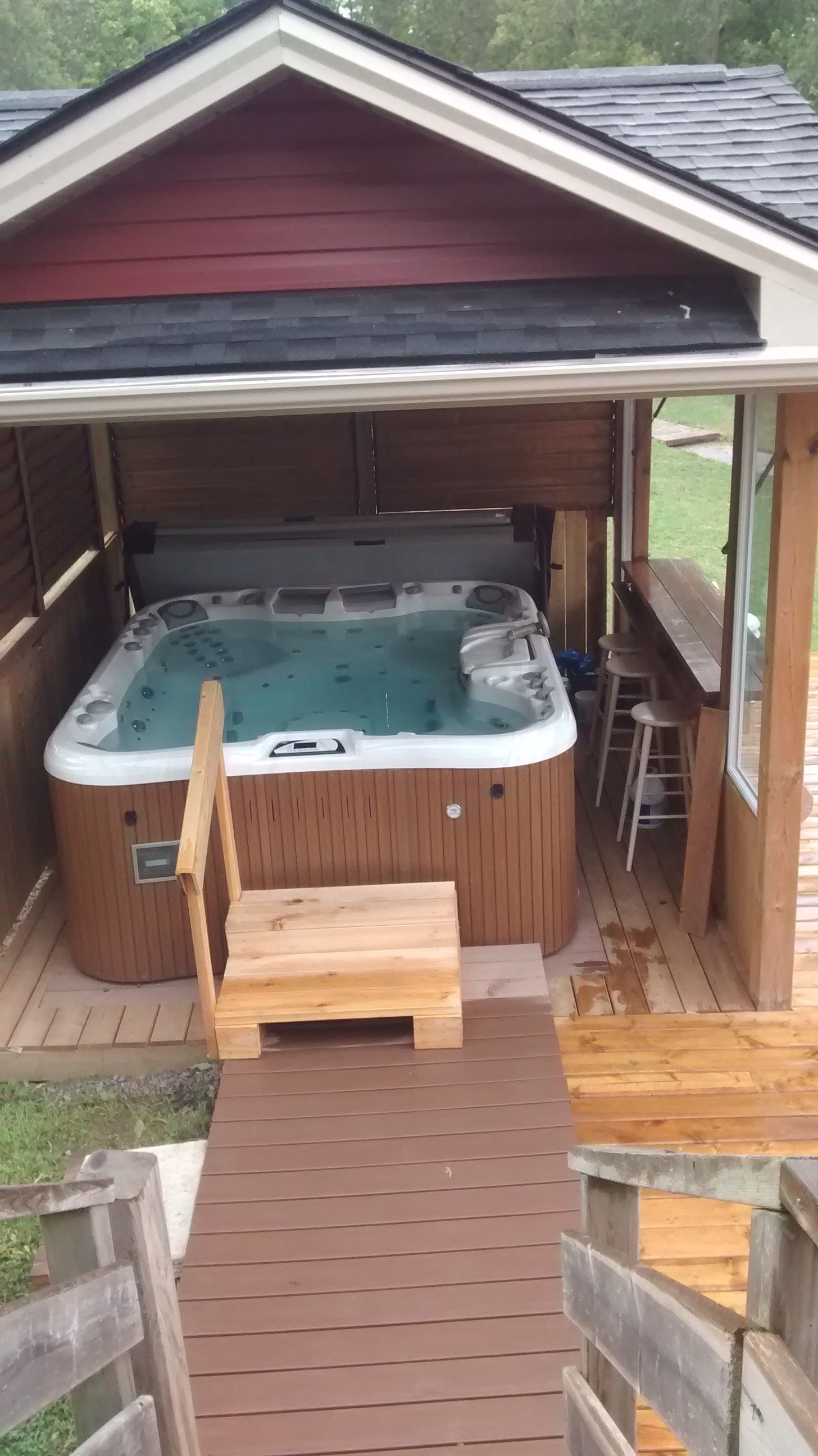 A hot tub is sitting under a gazebo on the deck of a house.