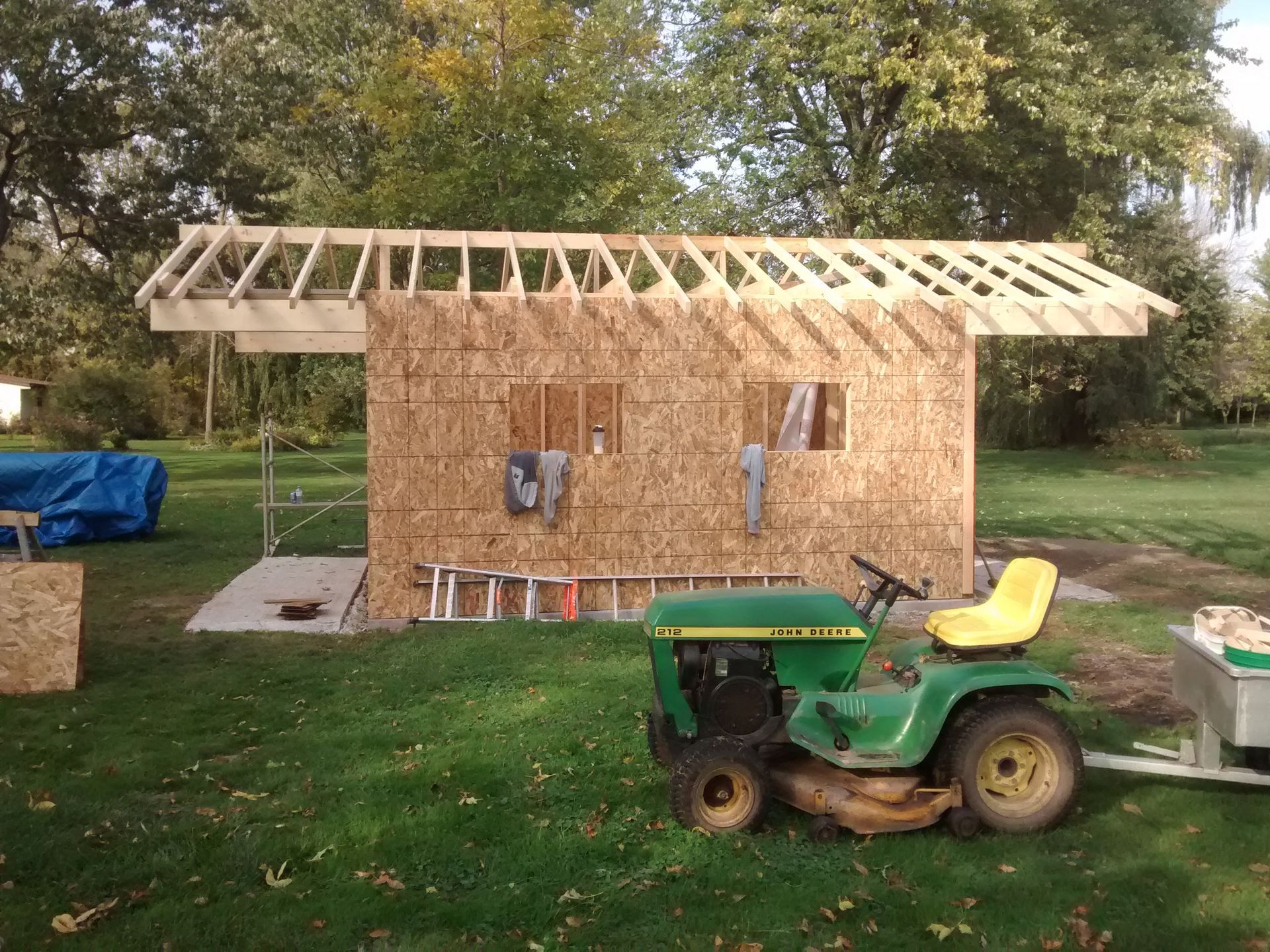 A john deere tractor is parked in front of a shed under construction.