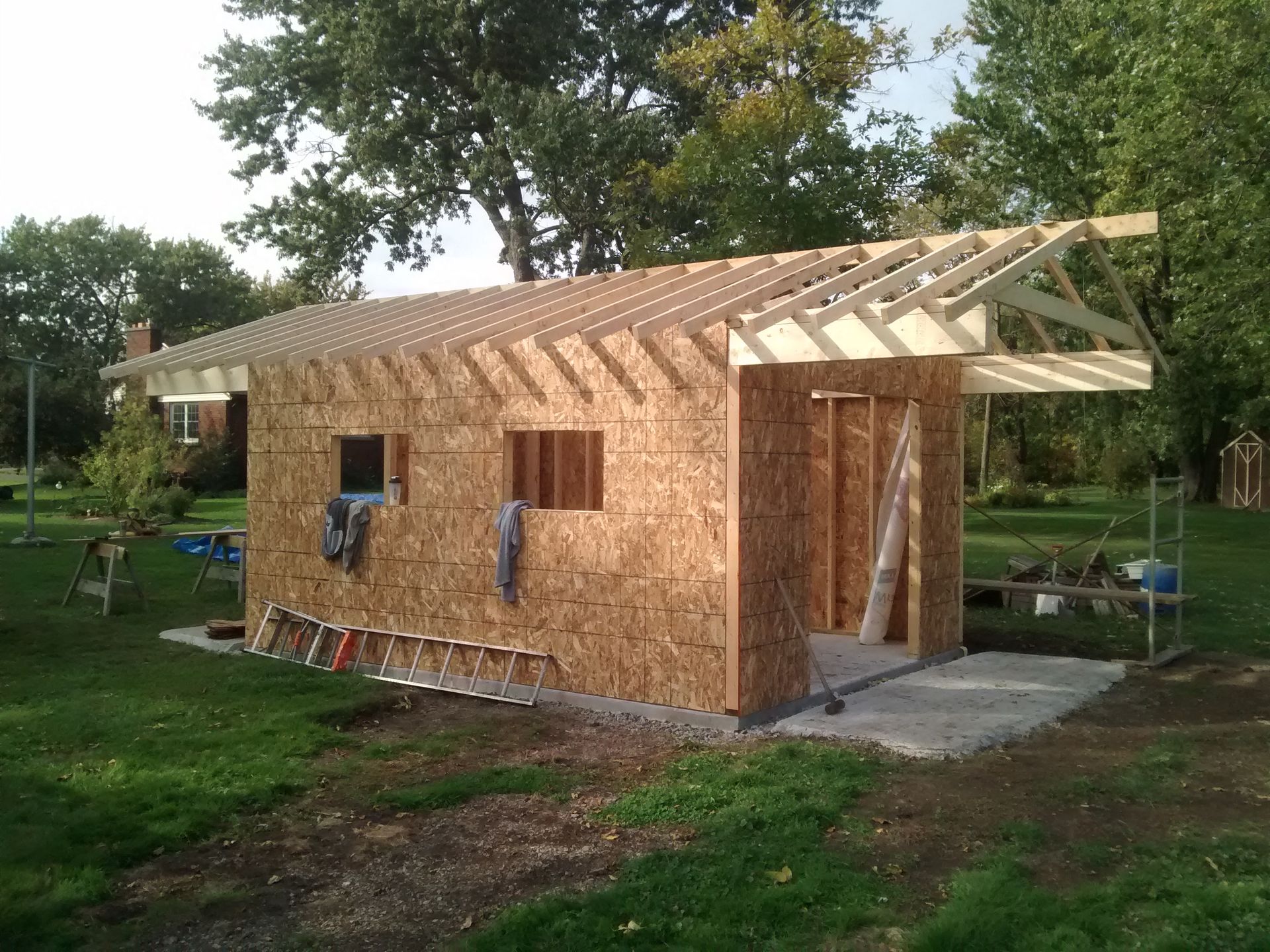 A shed is being built in a backyard with trees in the background