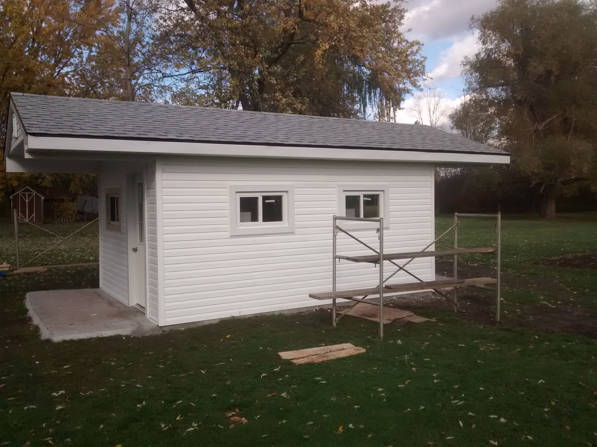 A white shed with a gray roof is in the middle of a grassy field