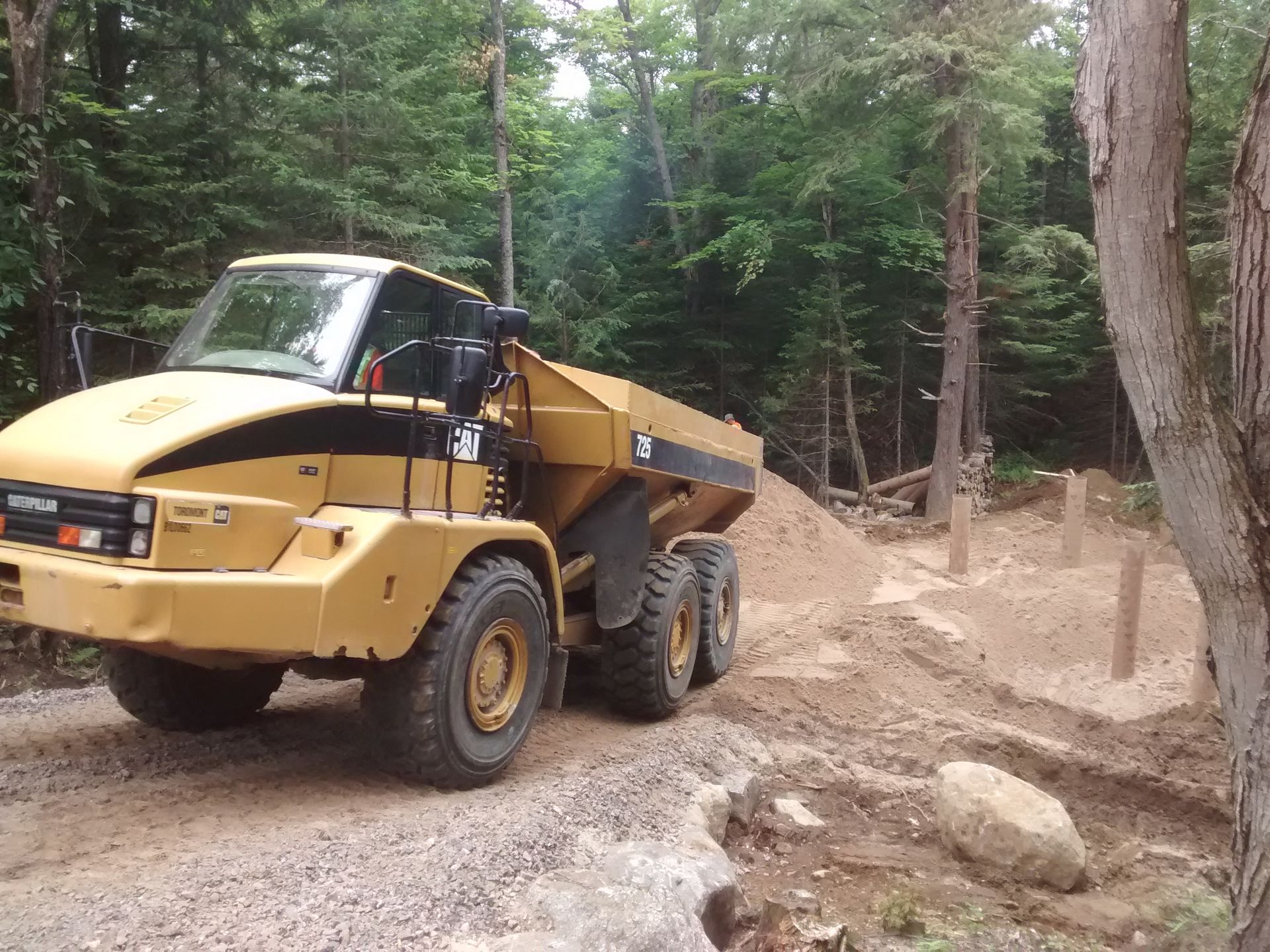 A dump truck is driving down a dirt road in the woods