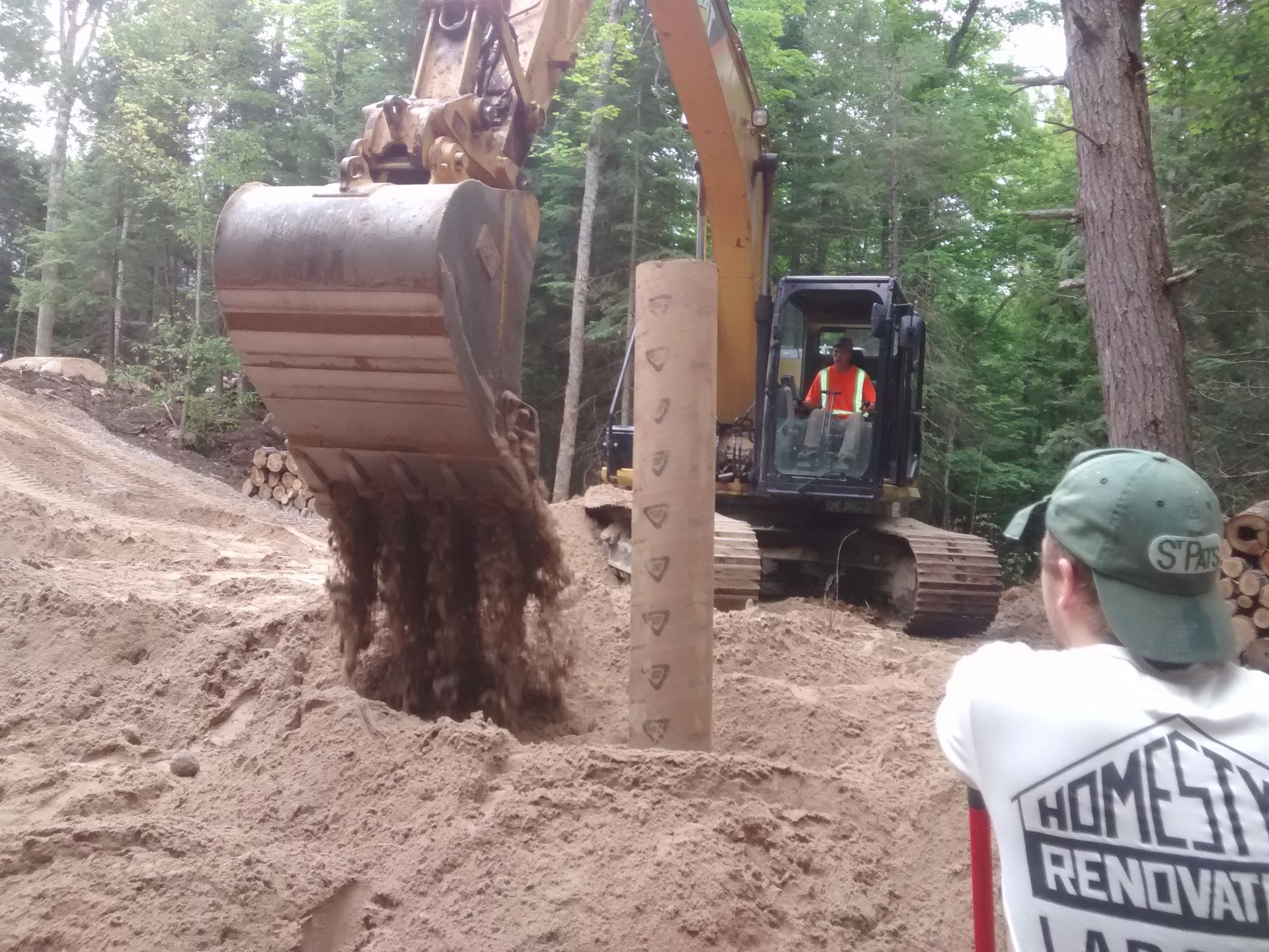 A man wearing a homestead renovations shirt stands in front of an excavator