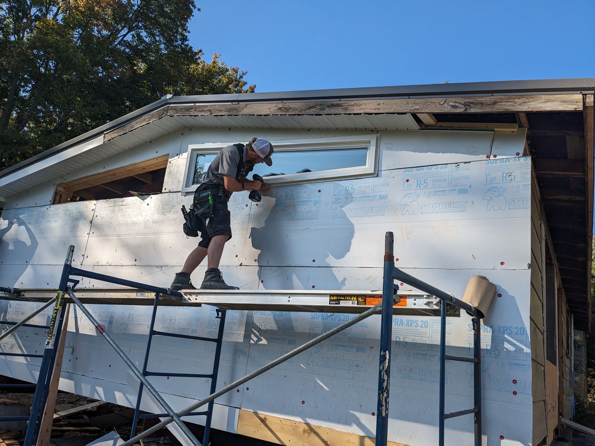 A man is standing on a scaffolding working on the side of a house.