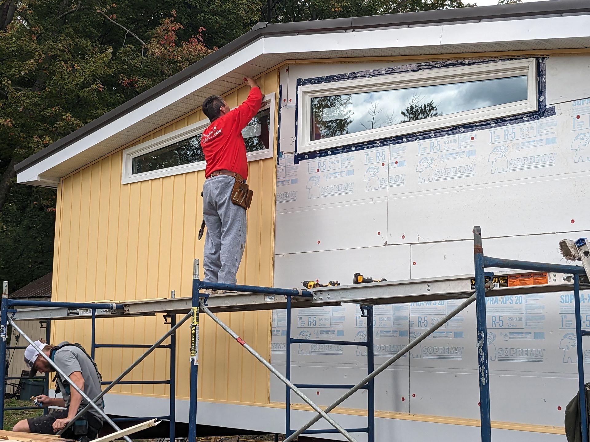 A man in a red shirt is standing on a scaffolding working on a house.