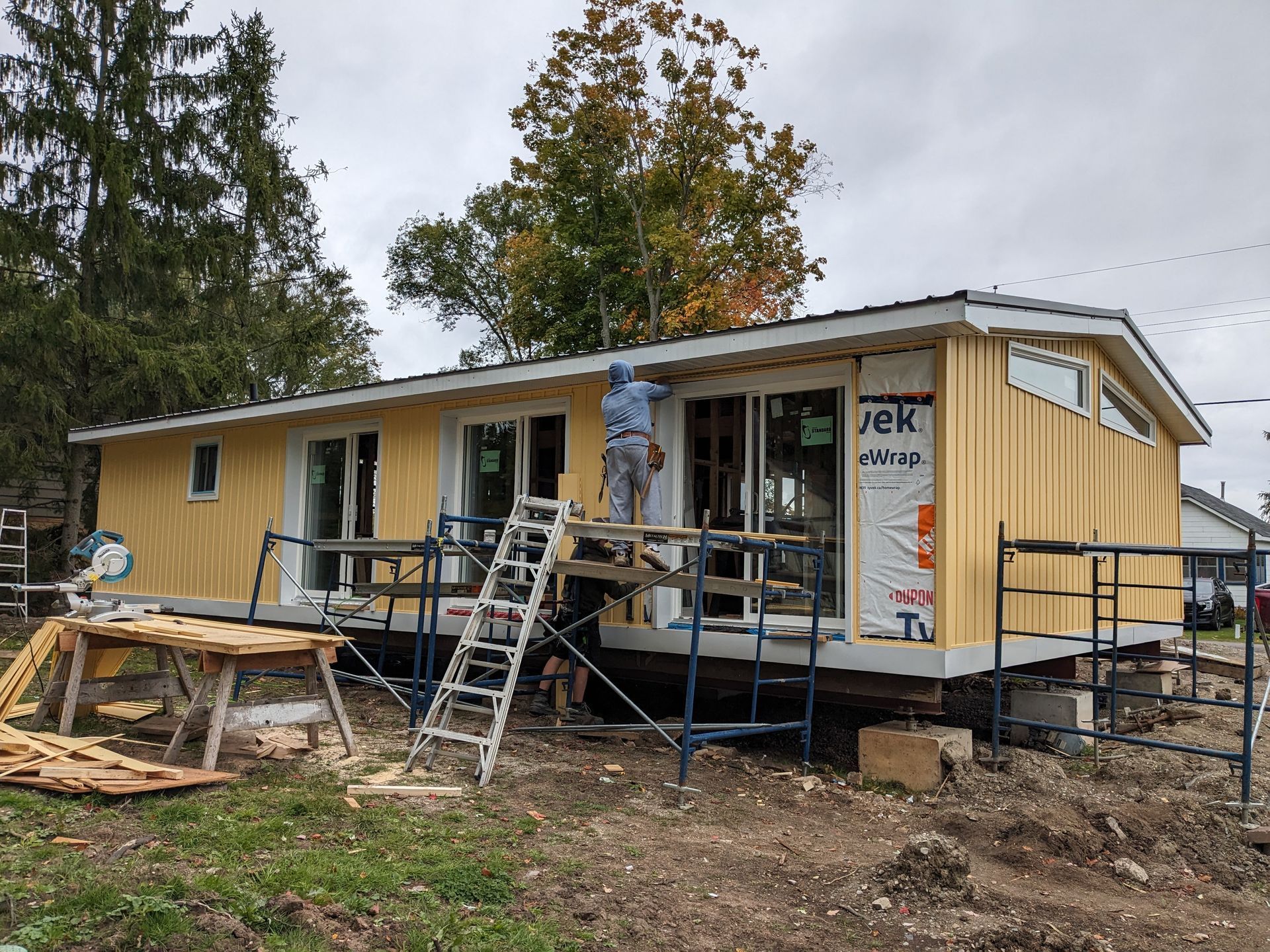 A man is standing on a ladder in front of a mobile home under construction.