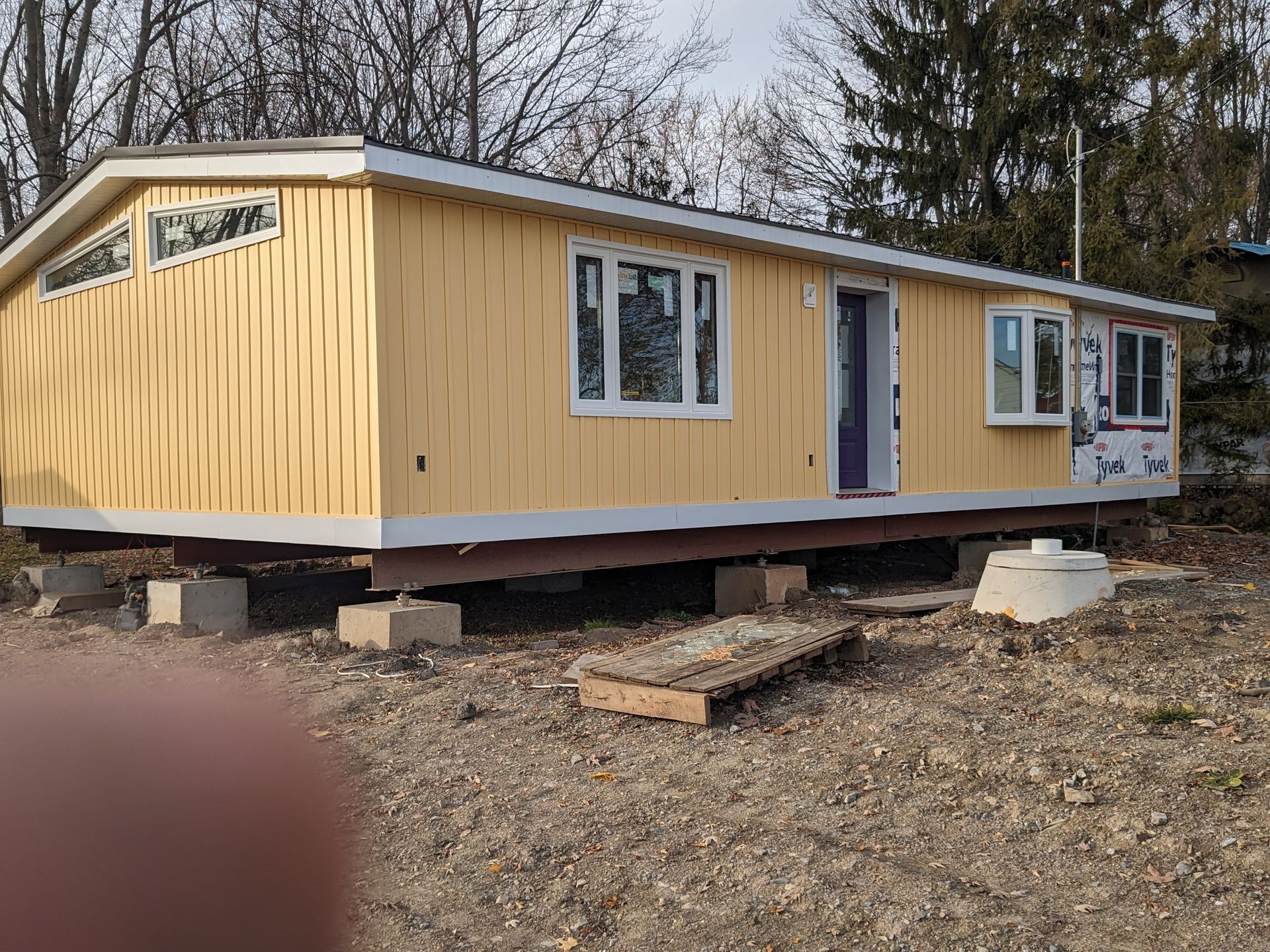 A yellow mobile home is sitting on top of concrete blocks in a dirt field.