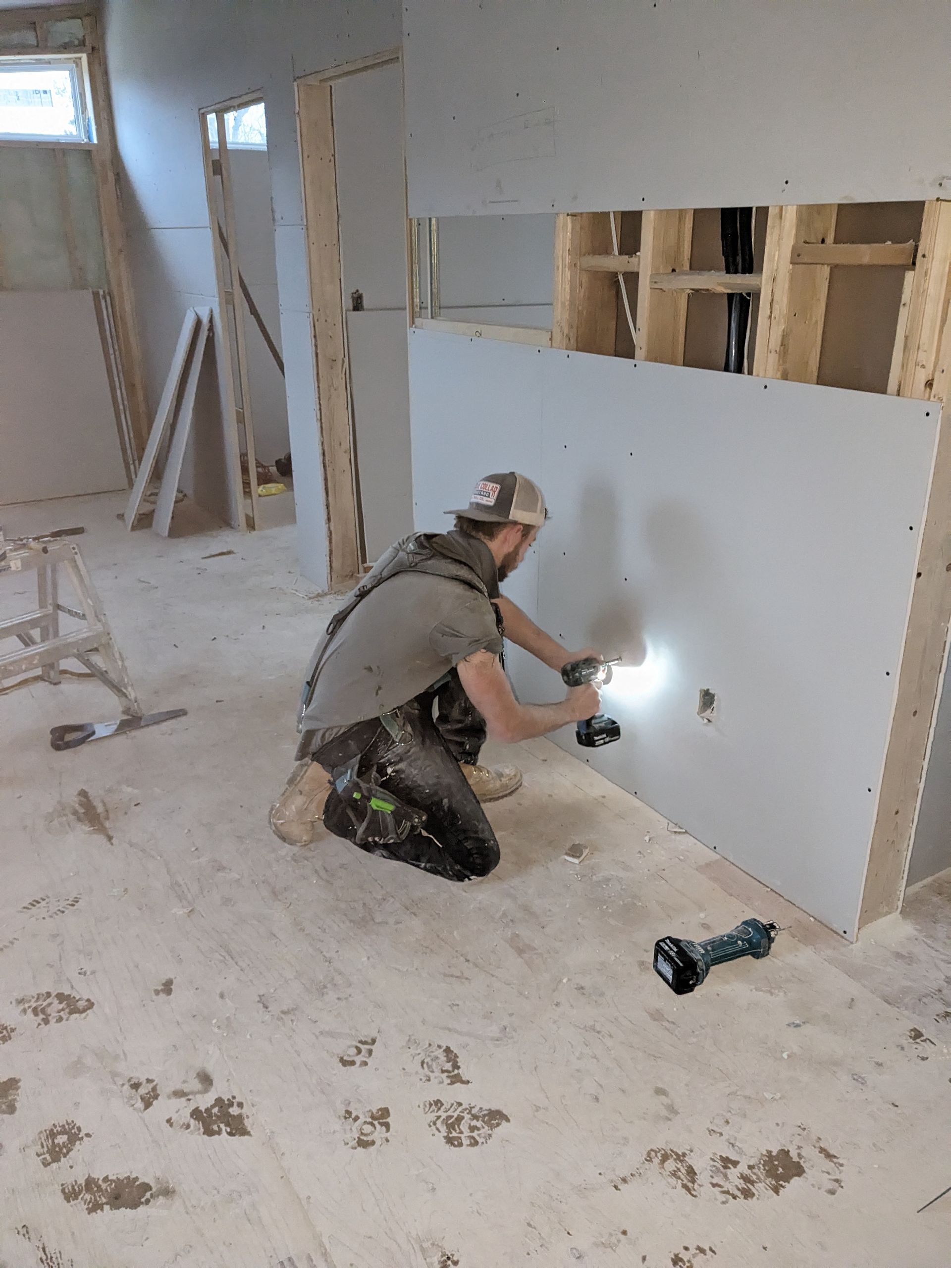 A man is kneeling down in a room while working on a wall.