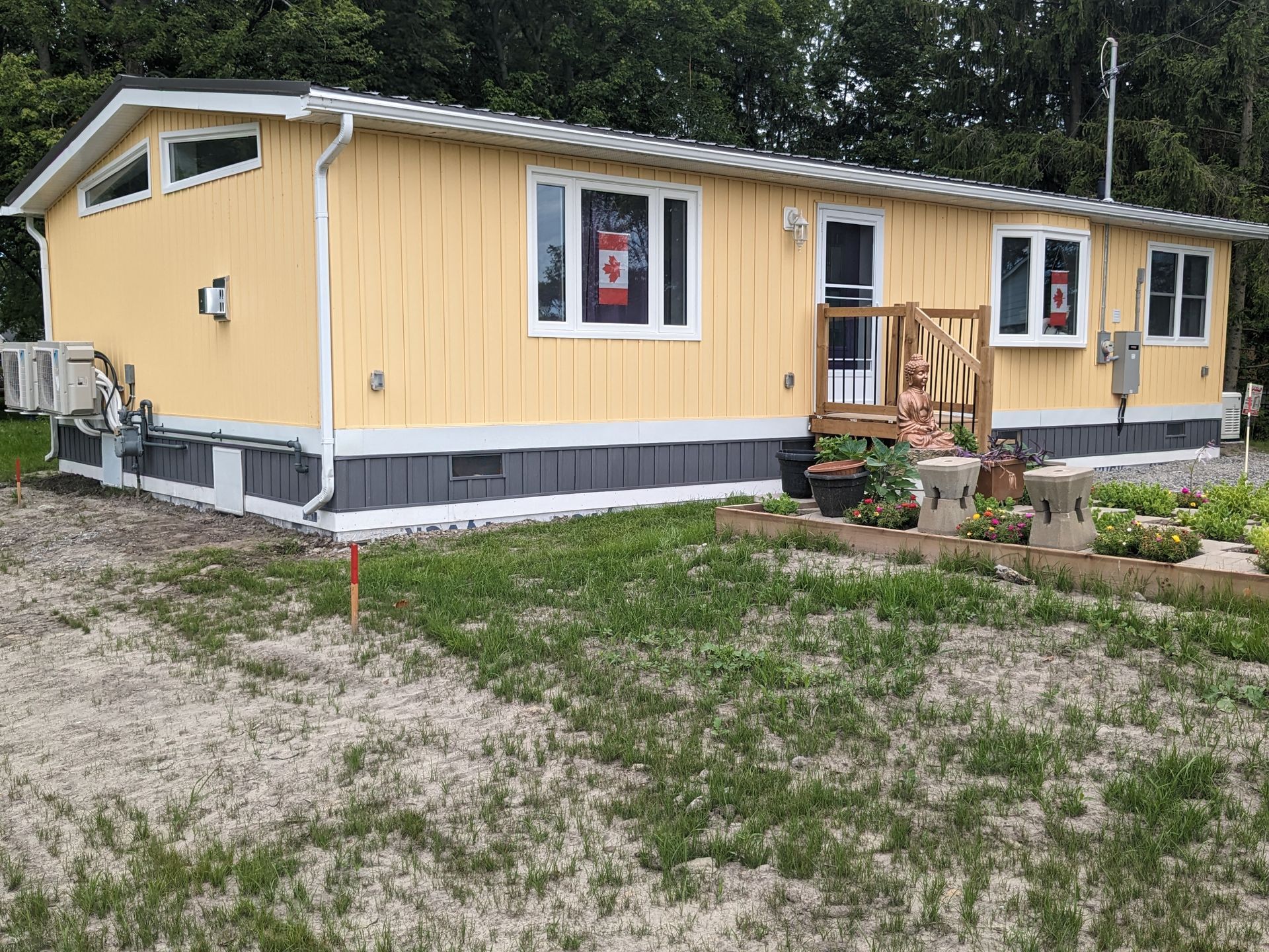 A yellow mobile home with a canadian flag on the front porch.
