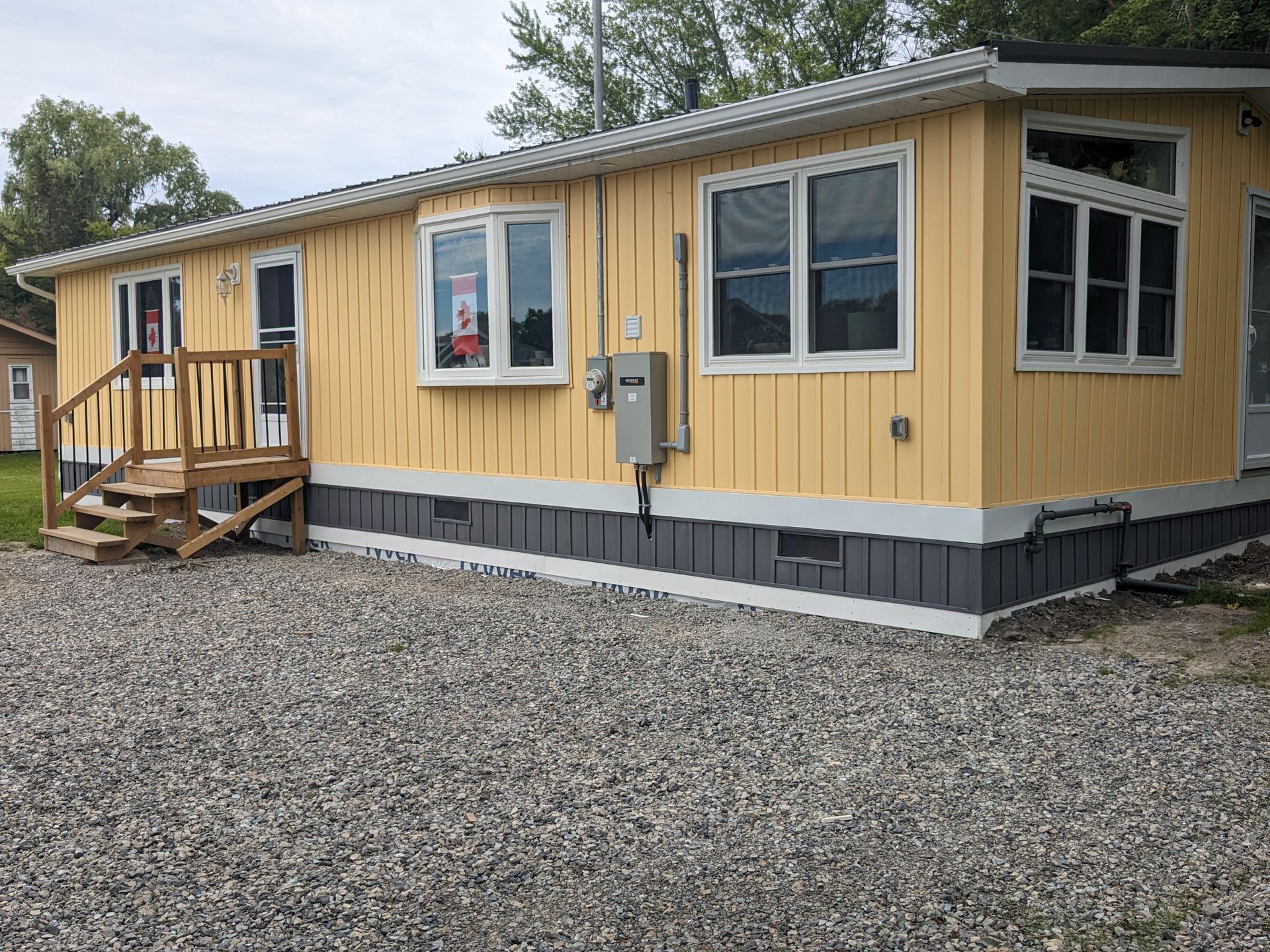 A yellow mobile home with a deck and stairs is sitting on top of a gravel lot.
