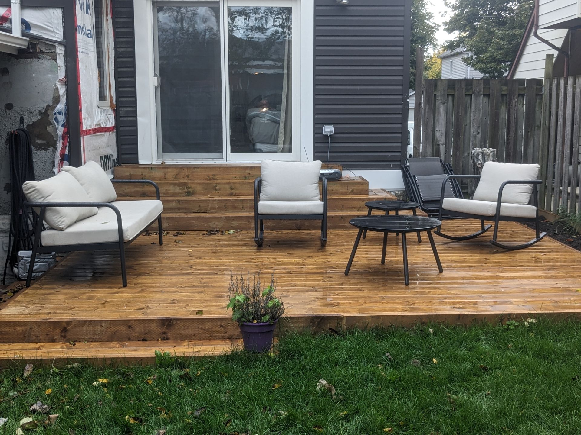 A wooden deck with a couch , chairs , and a table in front of a house.
